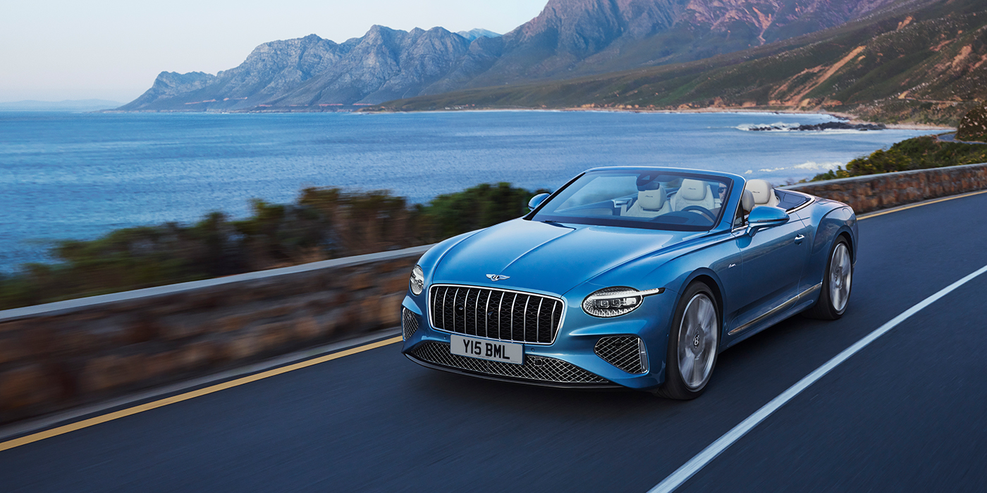 Bentley Rotterdam New Bentley Continental GTC Azure convertible in Light Windsor blue paint with 22 inch Azure wheels and chrome grill, driving dynamically by the sea