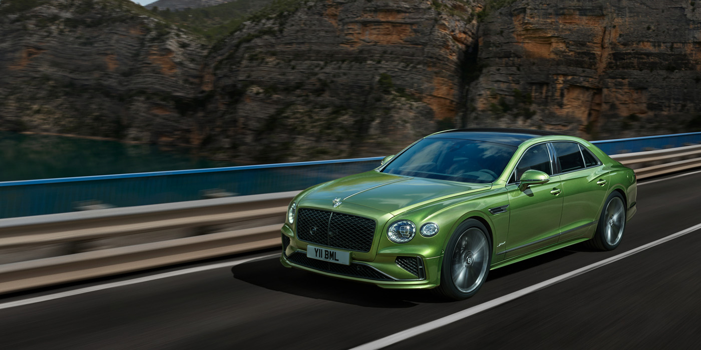 Bentley Rotterdam Bentley New Flying Spur Speed v8 hybrid sedan driving dynamically on a mountain road in Tourmaline Green paint