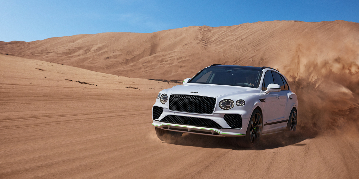 Bentley Rotterdam Bentley Bentayga Speed SUV front three quarter in Snow Quarts Pearlescent by Mulliner white paint driving dynamically through the desert