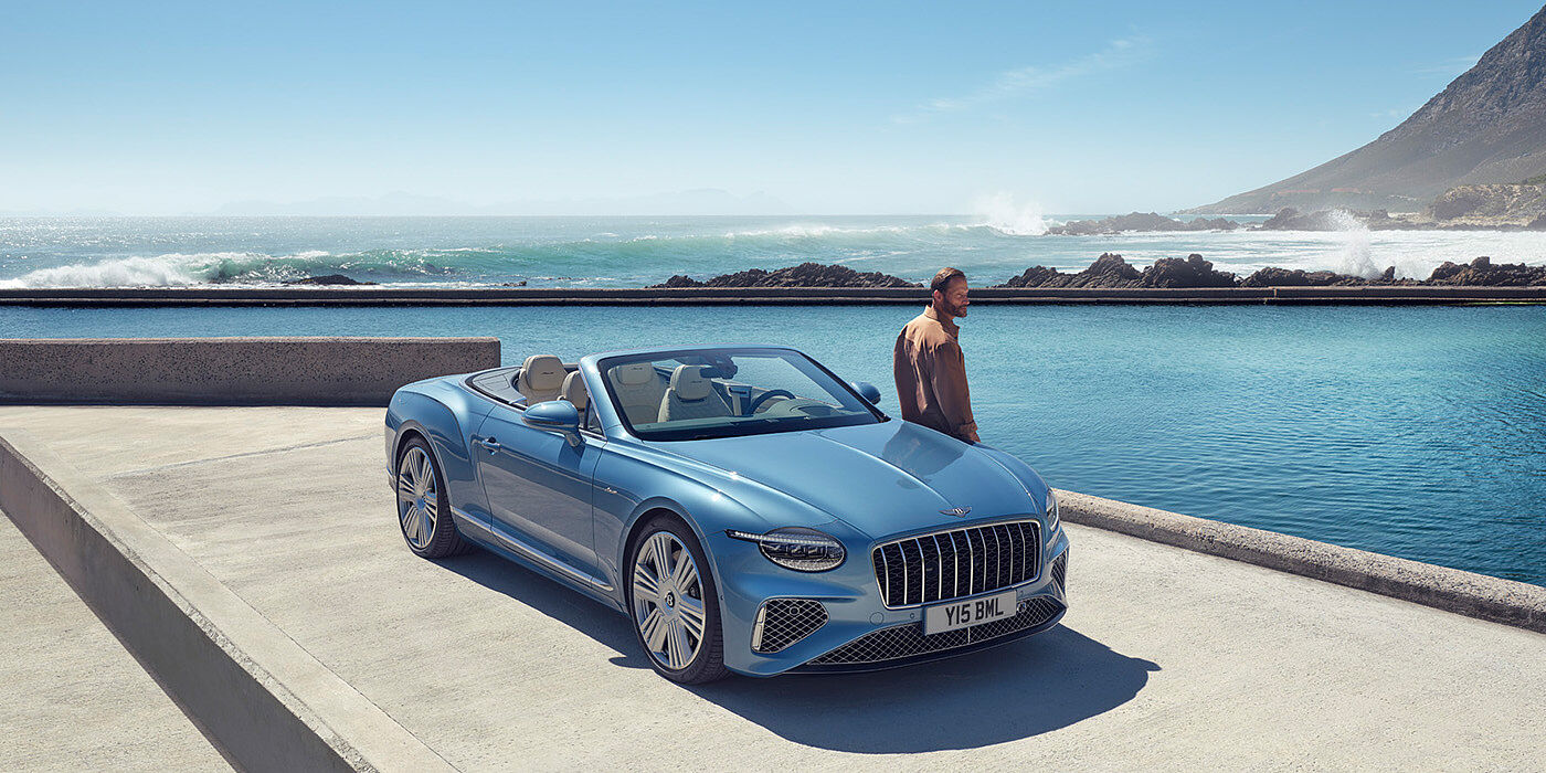 Bentley Rotterdam New Bentley Continental GTC Azure convertible front view in Light Windsor blue paint with 22 inch ten spoke wheels parked by the sea in the sunshine