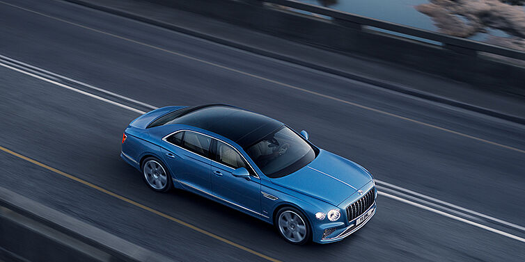 Bentley Rotterdam New Bentley Flying Spur Azure sedan in Light windsor blue paint by Mulliner, with 22 inch Azure wheels seen from overhead driving dynamically on a country road