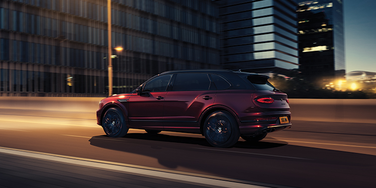 Bentley Rotterdam Bentley Bentayga Extended Wheelbase Mulliner SUV in Cricket Ball red paint driving dynamically in city at night